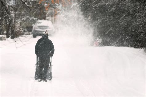 une personne utilisant un chasse-neige manuel pour dégager une allée enneigée
