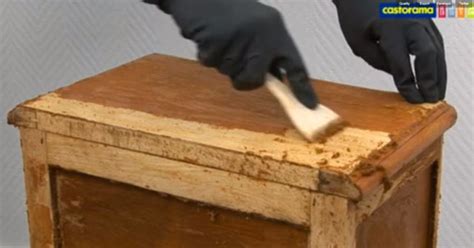 Un utilisateur appliquant du décapant sur un meuble en bois avec un pinceau.